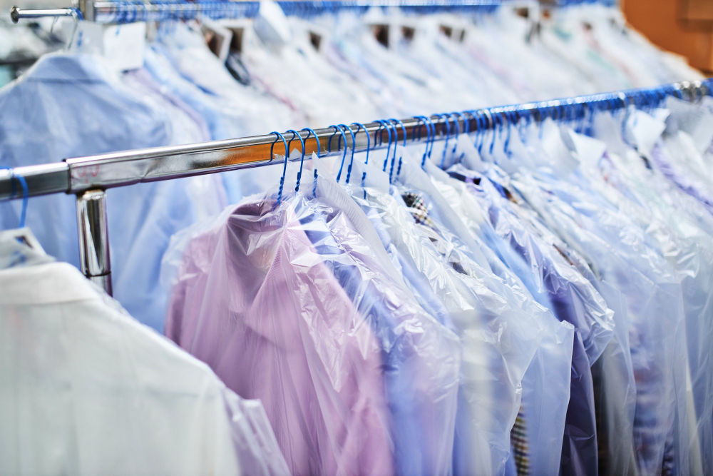 A row of shirts on hangers covered with clear plastic, hanging on a metal rack, likely in a dry cleaning facility.