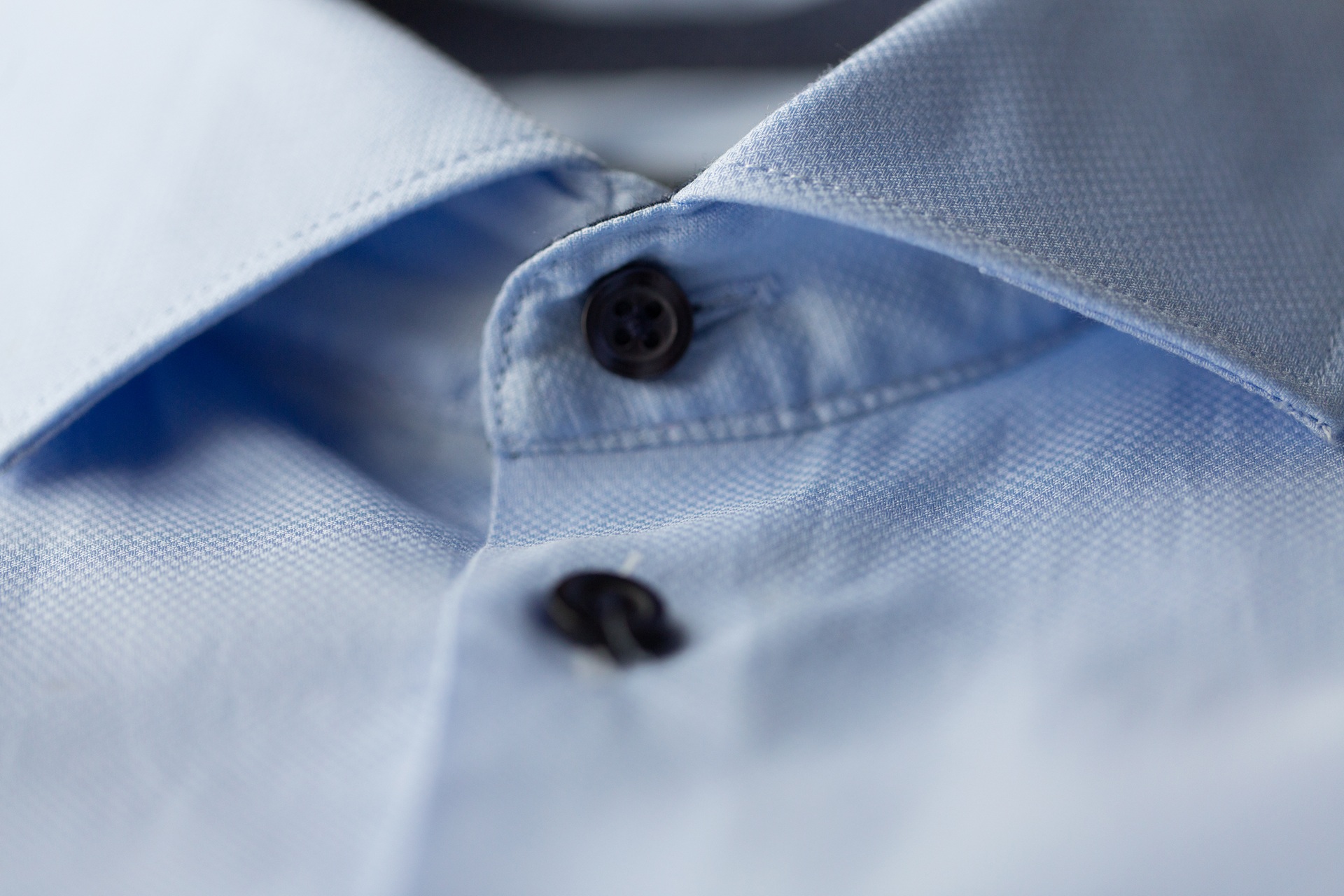 Close-up of a light blue collared shirt showing two black buttons, with the fabric texture and stitching details visible.