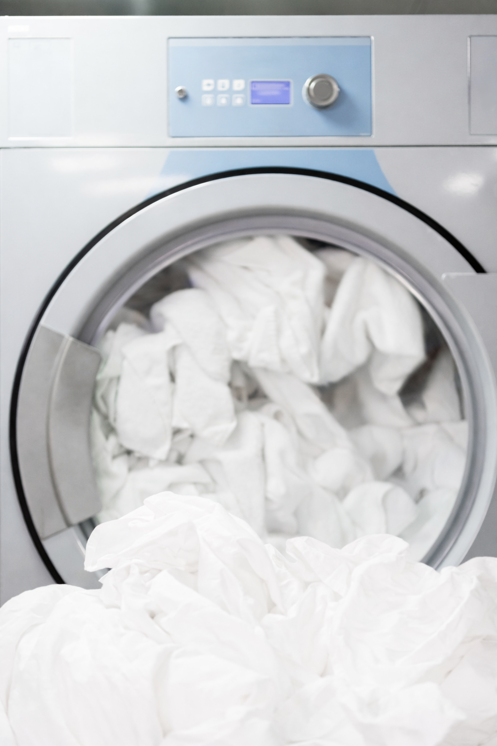A front-loading washing machine filled with white laundry, with additional white fabric in front of the machine.