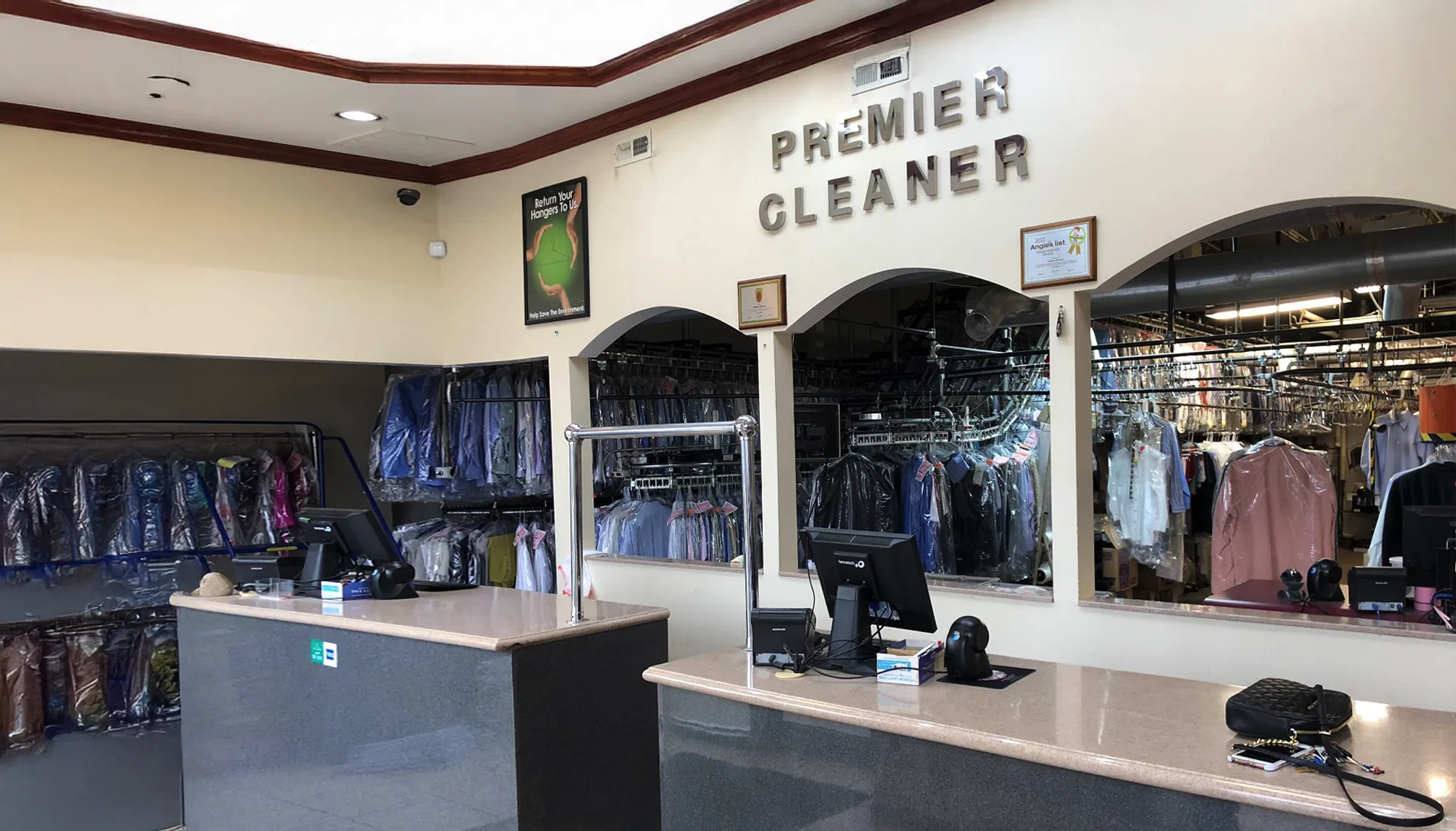 Interior of a dry cleaning shop with counters, computer terminals, and clothing on hangers behind glass labeled "Premier Cleaner.