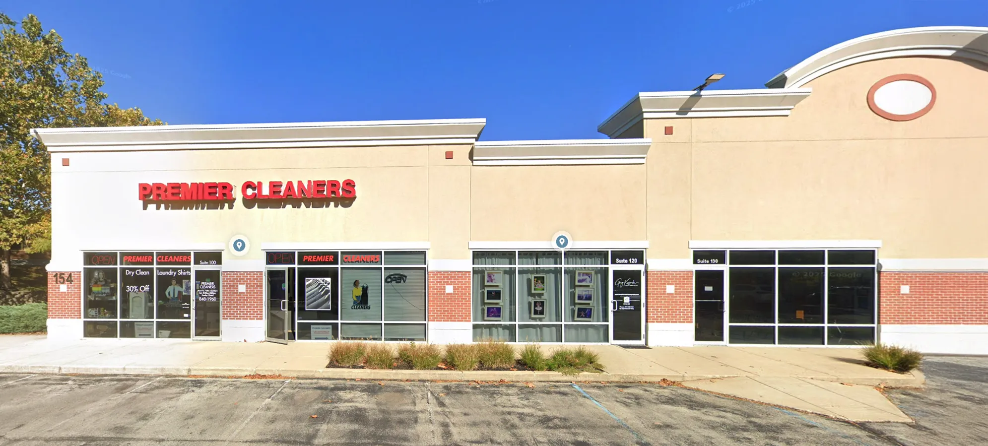 A beige and brick storefront with "Premier Cleaners" signage, large front windows, and a mostly empty parking lot under a clear blue sky.